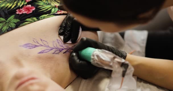 Tetovaný umělec má tetování s listy v rameni pro mladou ženu, zaostřená. — Stock video
