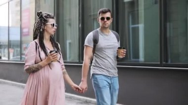 İki hipster erkeği ve hamile kadın şehirde el ele yürüyor.