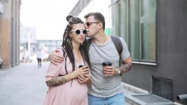 Çift hipsters adam ve hamile kadın kahve ile şehirde yürüyüş ve konuşma.