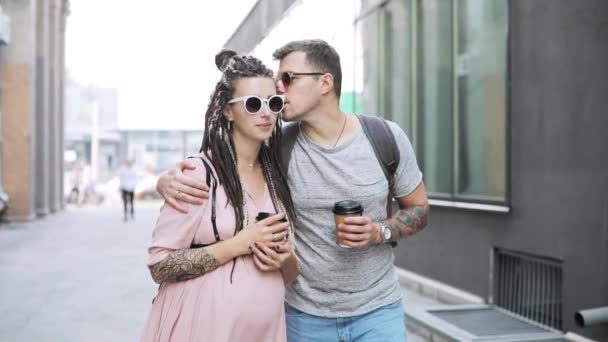Couple hipsters man and pregnant woman walking in city with coffee and talking. — Stock Video