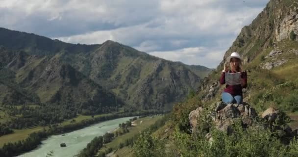 Kvinna vandrare sitter på toppen av Rocky Mountains lärande rutt på karta i dalen. — Stockvideo