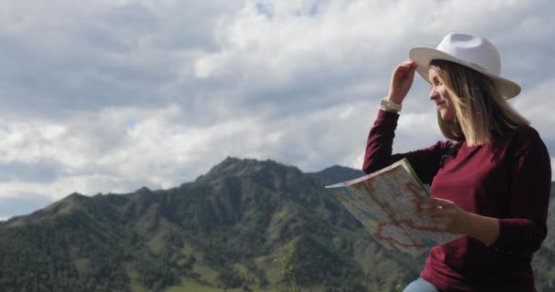 Жінка-мандрівник, що сидить на вершині скелястих гір, вивчає маршрут на карті . — стокове відео