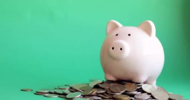 Kumbaraya bozuk para koyan adam yeşil arka plandaki bozuk para yığınının içinde duruyor..