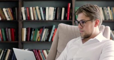 Gözlüklü adam portresi, arka plandaki kitaplıklarda bilgisayar üzerinde çalışıyor.