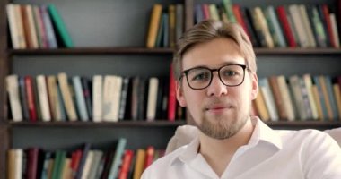 Üniversite kütüphanesinde kameraya bakan gözlüklü bir profesör ya da öğrenci..