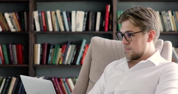 Portrét muže v brýlích pracuje na počítači v knihovnách na pozadí. — Stock video