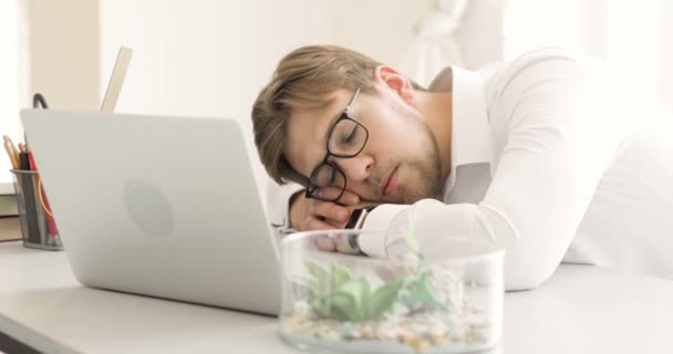 Hombre de negocios cansado durmiendo en la mesa cerca de la computadora portátil después de trabajar de noche en el arranque . — Vídeos de Stock