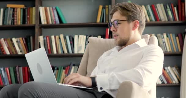 Człowiek pracuje na komputerze rozmawiając wideo czat i wpisując siedzi na krześle. — Wideo stockowe