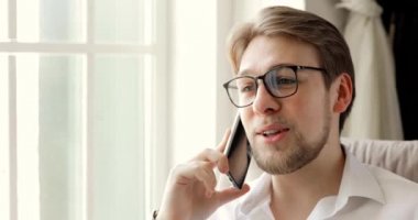 Akıllı telefondan konuşan mutlu bir adamın portresi pencerenin yanındaki koltukta oturuyor..