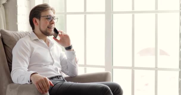 Mladý podnikatel mluví na smartphone sedí v křesle v kanceláři u okna. — Stock video