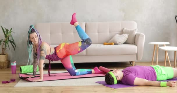 Woman doing sport exercise for legs on mat, man lying resting on mat near her. — Stock Video