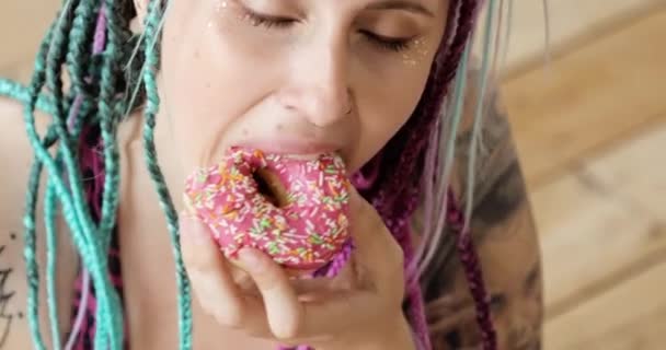 Retrato de la mujer disfrutando de comer donut en la alfombra de fitness en ropa deportiva en casa . — Vídeo de stock