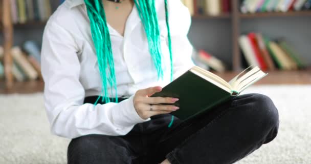 Oigenkännlig flicka med gröna dreadlocks hår läser en bok i biblioteket. — Stockvideo