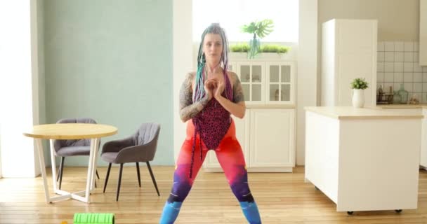 Mulher de sportswear colorido está fazendo agachamentos no treinamento de cozinha em casa . — Vídeo de Stock
