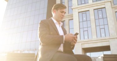 İşadamı işten sonra ofis binasının yanında oturan akıllı telefonlara bakıyor..