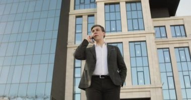 Genç işadamı şehir merkezindeki gökdelenin yanındaki akıllı telefondan konuşuyor..