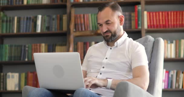 L'uomo sta parlando di videochiamata, chiacchierare seduto nel suo ufficio su scaffali sfondo. — Video Stock