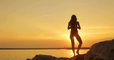 Mayolu kadın ağaç pozu veriyor güneş batarken deniz sahilinde yoga yapıyor..