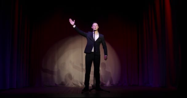 Homem de terno se levanta comediante falando piadas em microfone em pé no palco . — Vídeo de Stock