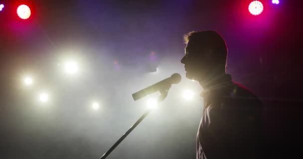Silhouette de l'homme debout comédien raconter des blagues dans le microphone sur scène. — Video