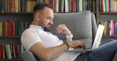 İşadamı dizüstü bilgisayarda çalışıyor. Ev ofisinin koltuğunda oturuyor..