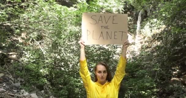 Mulher voluntária perto de tubo de esgoto na floresta com cartaz salvar o planeta em mãos . — Vídeo de Stock