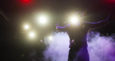 Showman sahnede el çırpıyor ve sahne ışıkları ve arka planda seyircileri eğlendiriyor..