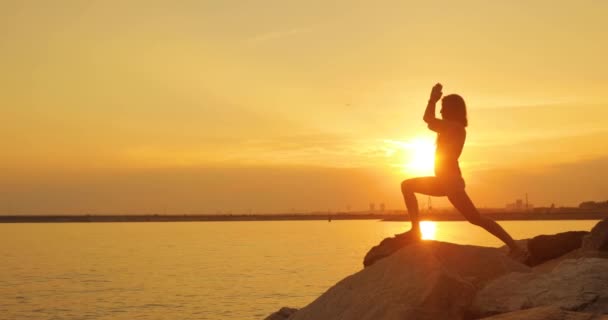 Vrouw in badpak is het maken van oefeningen oefenen yoga op zee strand bij zonsondergang. — Stockvideo