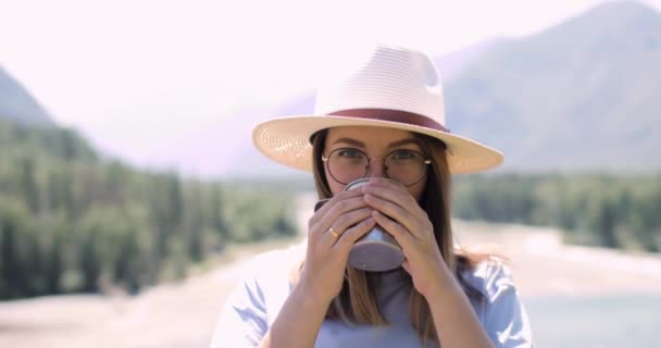 Молода жінка в капелюсі п'є чай в горах в літній сонячний день, вид спереду . — стокове відео