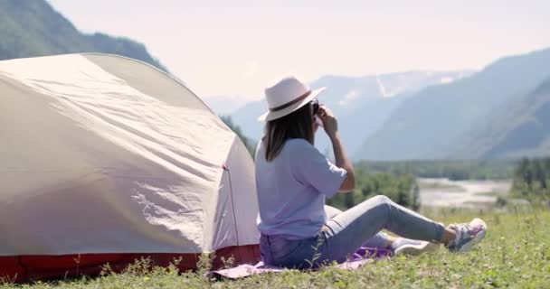 Kobieta turysta siedzi na górze w pobliżu namiotu pije herbatę podziwiając widok. — Wideo stockowe