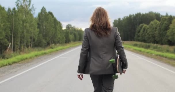 Hombre en traje de oficina con monopatín en las manos caminando por la calle fuera de la ciudad. — Vídeos de Stock