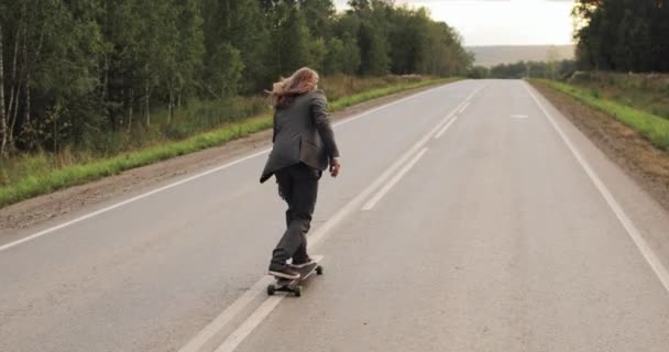 Muž v kancelářském obleku je jízda na skateboardu longboard po silnici mimo město. — Stock video