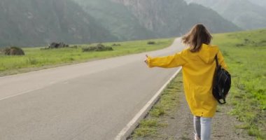 Otostopçu kadın asfalt yolda arabayı durdurmak için oy vermeye çalışıyor..