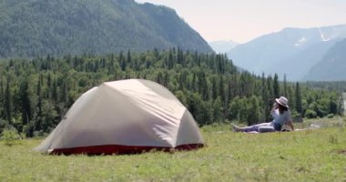 Çadırın yanındaki dağda oturan kadın yürüyüşçü çay içip manzarayı seyrediyor..