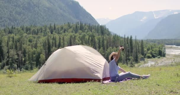 Donna turista è seduto sulla montagna vicino tenda e fare selfie su smartphone. — Video Stock