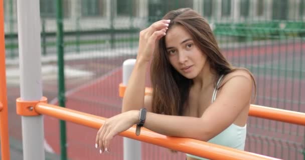 Retrato de mujer atlética cansada descansando en terreno deportivo y mirando a la cámara. — Vídeo de stock