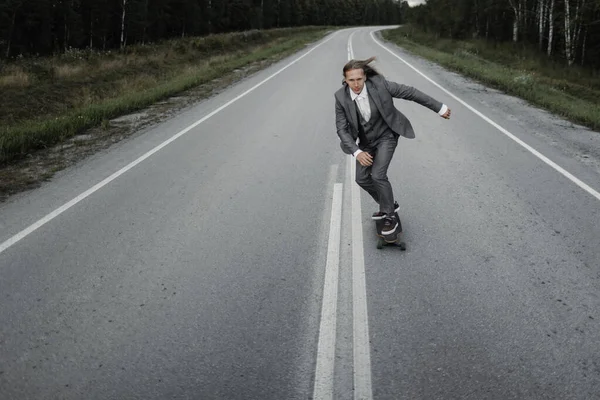 Homem em terno de escritório está montando skate longboard estrada abaixo fora da cidade . — Fotografia de Stock