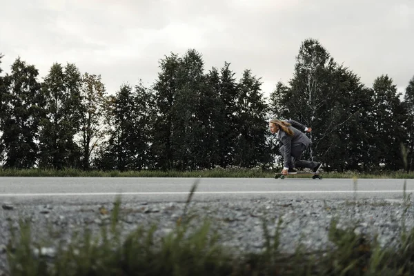 Homem em terno de escritório está montando skate longboard estrada abaixo fora da cidade . — Fotografia de Stock