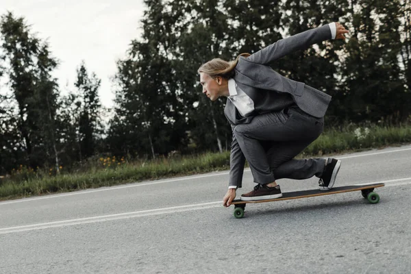 Homem em terno de escritório está montando skate longboard estrada abaixo fora da cidade . — Fotografia de Stock