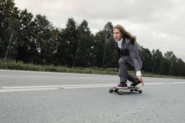 Homem em terno de escritório está montando skate longboard estrada abaixo fora da cidade . — Fotografia de Stock