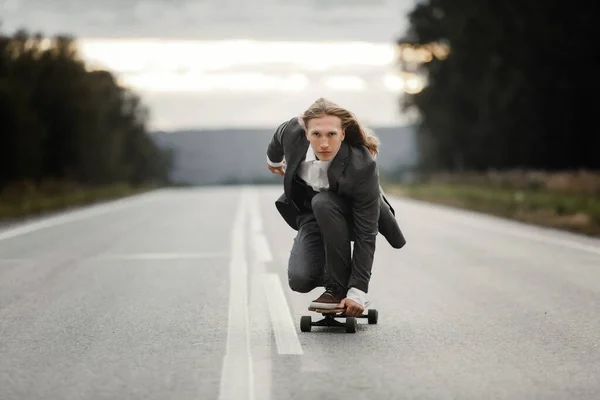 Man i kontorsdräkt rider skateboard longboard nerför vägen utanför staden. — Stockfoto