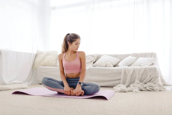 Spor giyimli genç kız yoga yapıyor ve evinde esneme hareketleri yapıyor..
