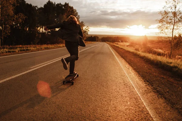 Άντρας με κοστούμι γραφείου ιππεύει skateboard longboard κάτω από το δρόμο έξω από την πόλη. Εικόνα Αρχείου