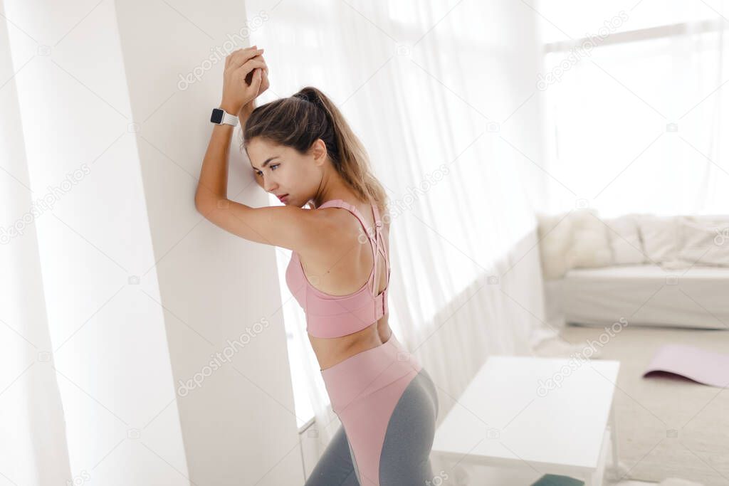 young sports girl in sportswear is doing yoga and stretching at home in a bright room.