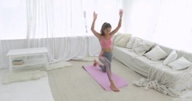 Atletik genç kadın evdeki oturma odasında hareketli savaşçı yoga pozu veriyor..