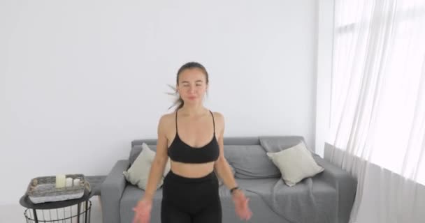 Femme fait saut jeg exercice sur le tapis dans le salon, caméra se déplace loin. — Video