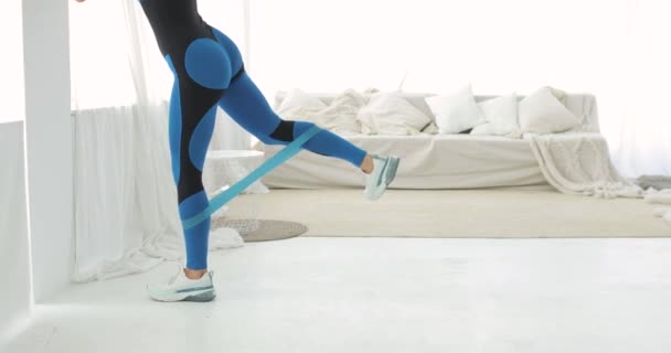 Γυναίκα κάνει άσκηση για γλουτούς χρησιμοποιώντας λαστιχένια ταινία στο σπίτι, πόδια closeup. — Αρχείο Βίντεο