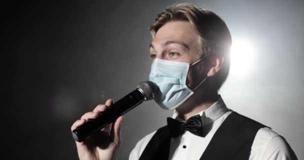 Showman host of event in medical mask speaks at microphone at concert on stage. — Stock Footage Showman host of event in medical mask speaks at microphone at concert on stage. Royalty Free Stock Footage