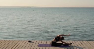 Bacağa yaslanan bir kadın nehir kıyısındaki ahşap iskelede oturuyor..