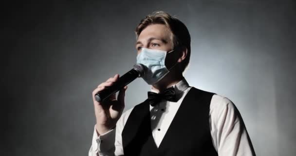 Portrét showman hostitel akce v lékařské masce mluví u mikrofonu na koncertě. — Stock video